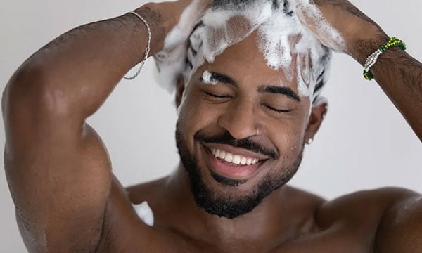 A man in the shower smiling and washing his hair