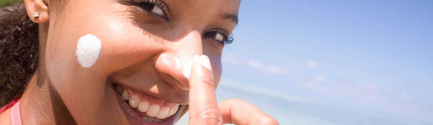 A woman smiling and applying sun cream to her face