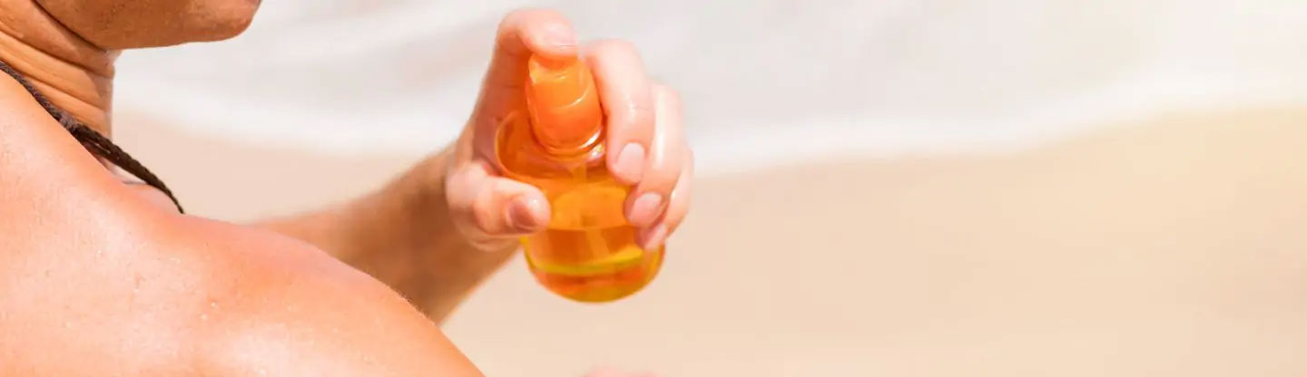 A man applying sun tan lotion from a spray bottle