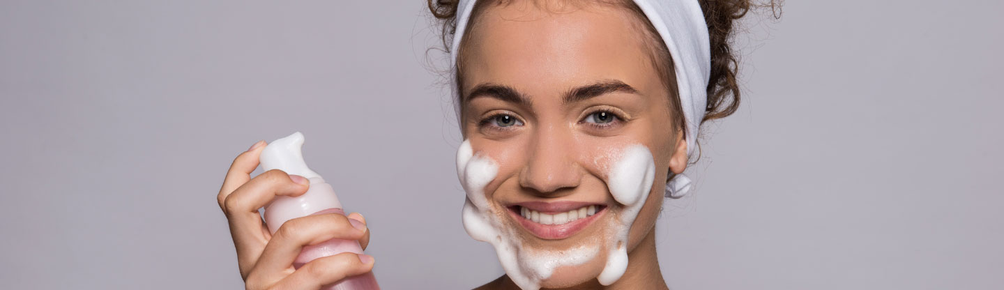 A smiling woman applying foaming face soap