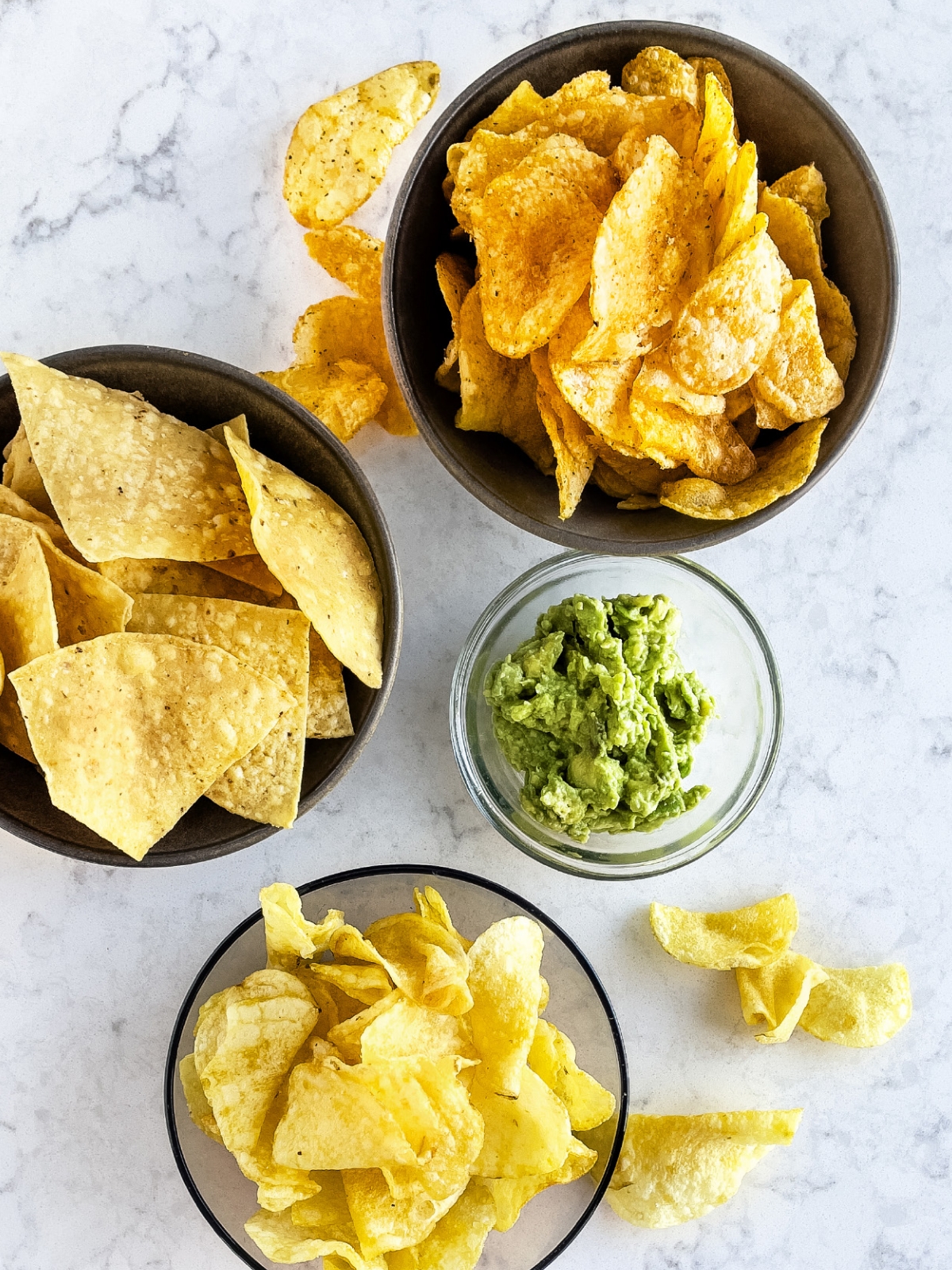 Three bowls of chips surrounding a bowl of guacamole