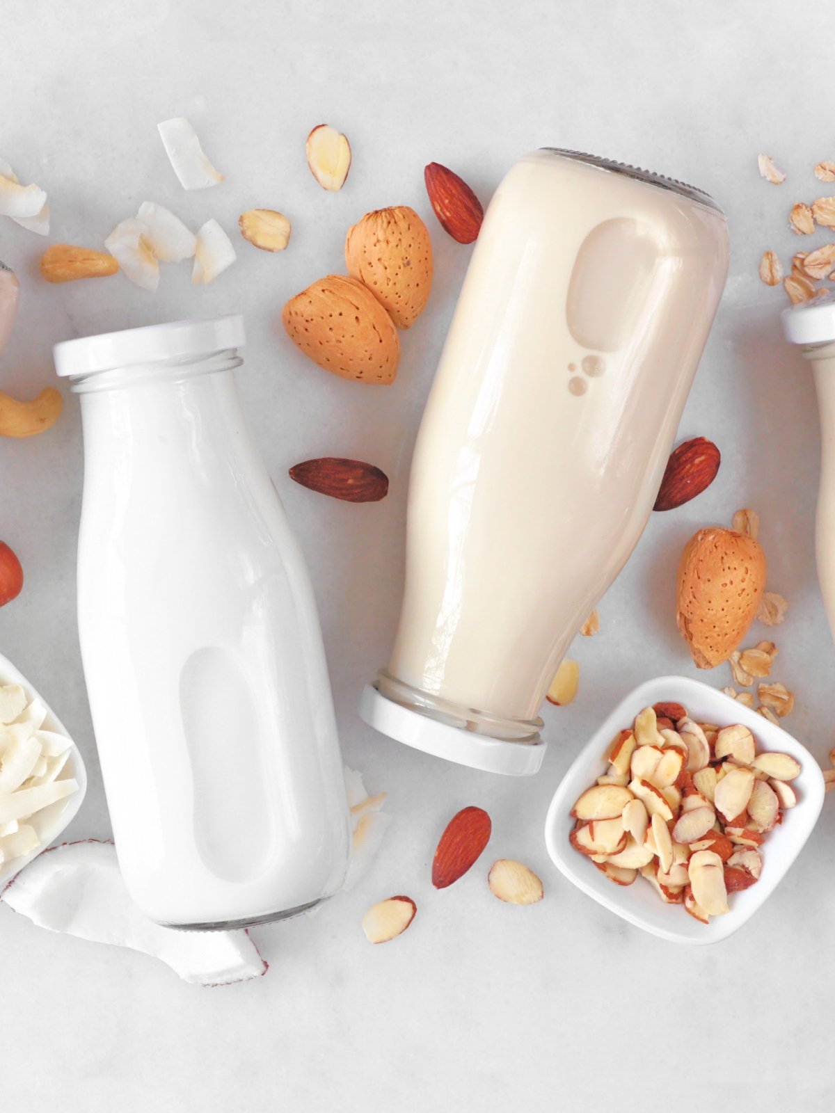 Reuseable glass bottles of plant-based milk on a table with nuts