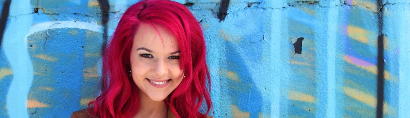 Pink haired woman stood by a wall
