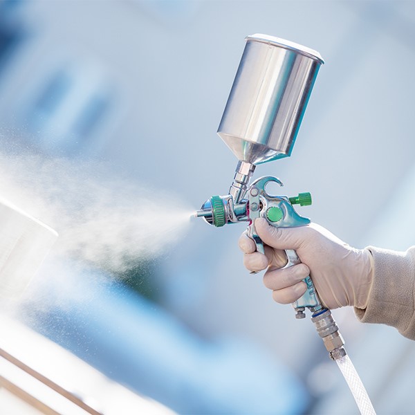 Hand holding an air compression sprayer misting sustainable coatings