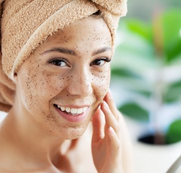 Woman applying face scrub to her face wearing a towel