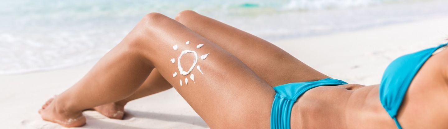 Woman lying on a beach with a sun drawn on her leg in sun cream