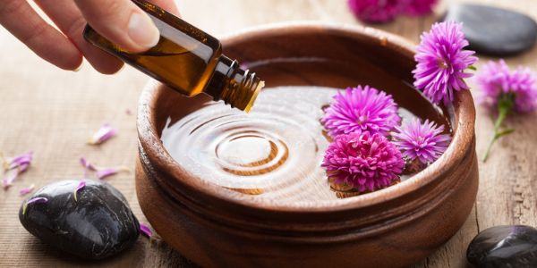 Essential oils being dropped into a bowl of flowers