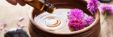 Essential oils being dropped into a bowl of flowers