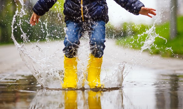 Water splashes up as a child jumps in a water puddle wearing yellow rubber boots