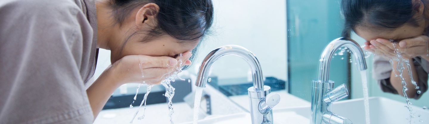 Woman washing her face with water over a sink