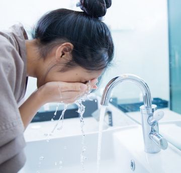 Woman washing her face with water over a sink