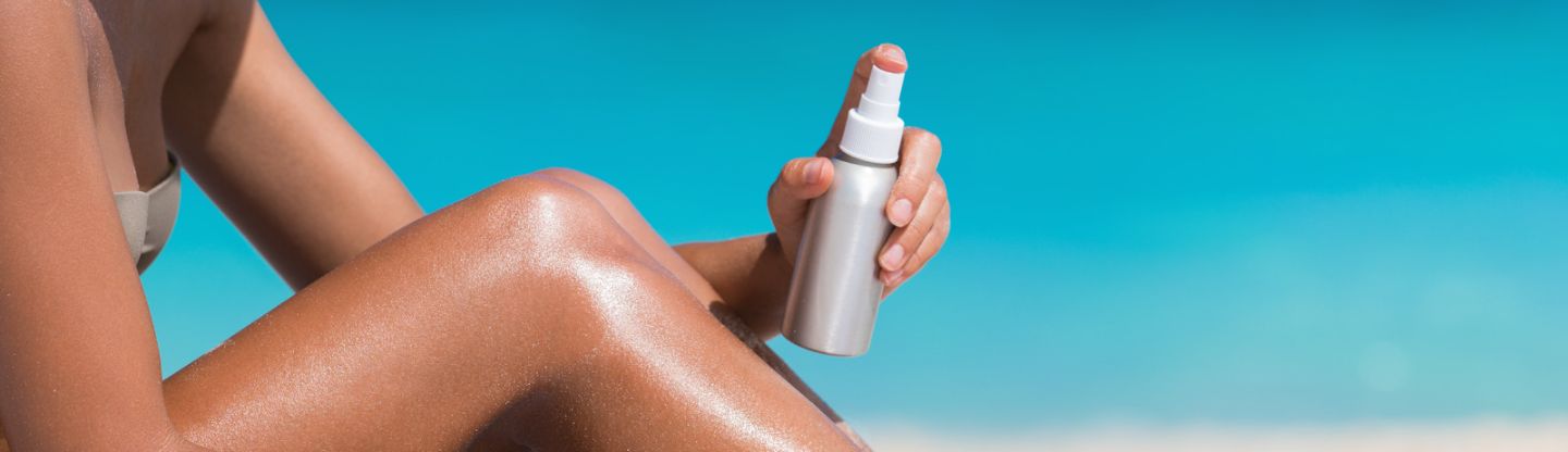 A person spraying sun lotion on their legs