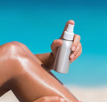 A person spraying sun lotion on their legs