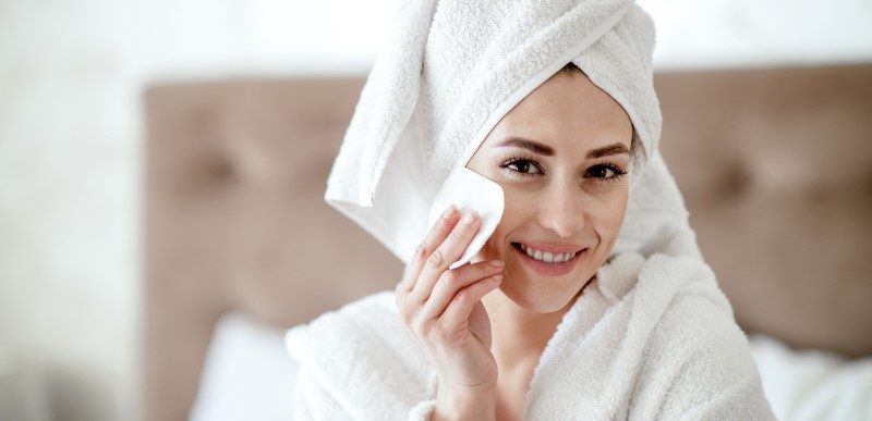 Woman in bathrobe washing face with nature inspired make-up remover